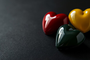 Wall Mural - Three hearts in red, yellow, and green colors arrange on black background, top view, copy space