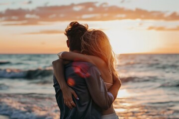 Two people share an intimate moment hugging each other tightly with a beautiful sunset over the ocean as a backdrop