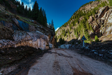 Poster - Dirt road in high mountains in spring, melting deep snow on edge of road