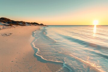 Golden sunset illuminating sandy beach with gentle waves crashing on shore