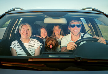 Happy family enjoys road trip together, with fluffy brown Maltipoo dog in front seat and two young girls in back. Scene captures the joy and warmth of family outing in their car