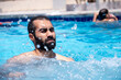© Viga - Young bearded male enjoys water splash under the heat of the sun having wonderful time with friends during vacation in summer