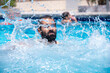© Viga - Young bearded male enjoys water splash under the heat of the sun having wonderful time with friends during vacation in summer