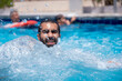 © Viga - Young bearded male enjoys water splash under the heat of the sun having wonderful time with friends during vacation in summer