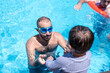 © Viga - A young father is helping his child begin swimming, teaching him the basics and ensuring he isn't afraid of drowning or getting water in his ears, mouth, and nose
