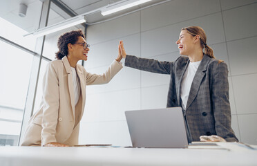 Successful business people giving each other a high five while working on laptop in coworking