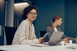 © Kostiantyn - Young business woman working on laptop and use phone while sitting in office and looks camera