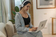 © aFotostock - Happy asian woman use headphones listen to music online web conference sitting on cozy sofa in living room at home. Female asian people working at home research watching online e-learning video call
