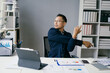 © Parichat - Business Professional Stretching at Desk in Modern Office with Documents and Digital Devices