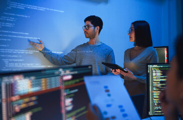 Wall Mural - asian developer leads present code review session, pointing at code projected on the wall with colleagues  teamwork and knowledge sharing in software development.