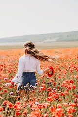 Canvas Print - Happy woman in a poppy field in a white shirt and denim skirt with a wreath of poppies on her head posing and enjoying the poppy field.