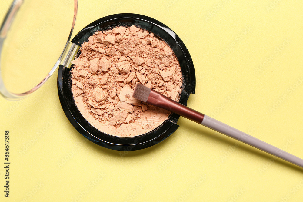 Makeup brush and facial powder on yellow background