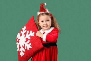 Wall Mural - Cute little girl in Santa Claus costume with beautiful Christmas cushion on color background