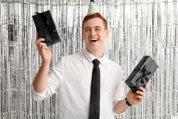 Wall Mural - Young man in party hat with gift boxes celebrating Birthday on tinsel background