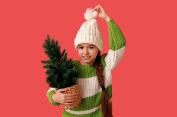 Canvas Print - Cute little girl wearing warm hat with Christmas tree in pot on red background