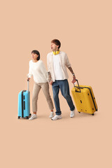 Wall Mural - Couple of young tourists with suitcases running on beige background