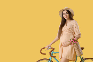 Poster - Young pregnant woman with bicycle on yellow background