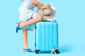 Wall Mural - Female traveler with suitcase and beach accessories on blue background