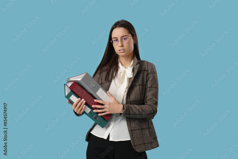 Tired young businesswoman with office folders on blue background