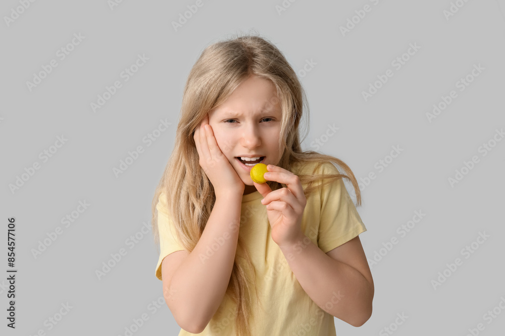Young girl eating cookie and suffering from toothache on grey background