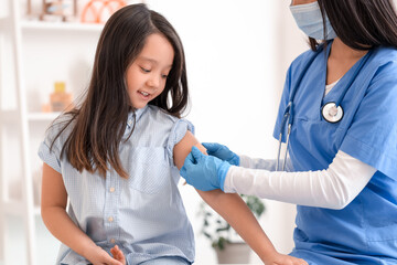 Canvas Print - Little Asian girl with doctor applying patch after vaccination in clinic