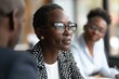 © Anton Gvozdikov - Confident businesswoman wearing glasses attentively listens during a meeting with colleagues in an office setting.