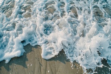 Wall Mural - An aerial closeup of ocean waves crashing on a sandy shore. The white foam of the waves is contrasted against the tan sand