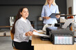 © Pixel-Shot - Young businesswoman with her colleague printing document at table in office