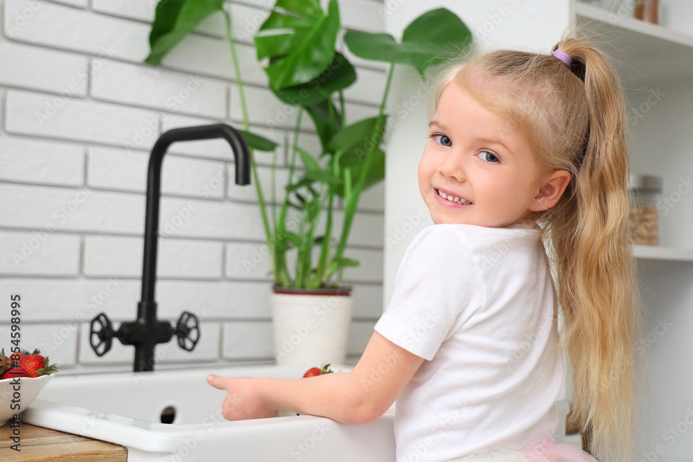 Little girl washing strawberries in kitchen