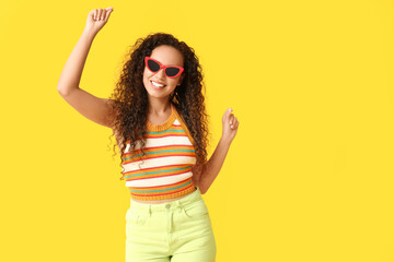 Wall Mural - Happy young African-American woman in sunglasses on yellow background