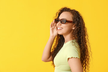 Wall Mural - Happy young African-American woman in sunglasses on yellow background