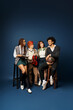 © LIGHTFIELD STUDIOS - A group of young multicultural friends, including a nonbinary person, sitting closely next to each other in stylish attire on a dark blue background.