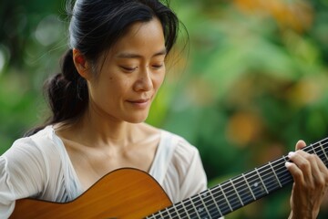 Wall Mural - Portrait of a blissful asian woman in her 30s playing the guitar in soft green background