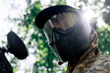 close up in the wild crouching near the trees player in a pinball uniform holds a gun with paint balls demonstrating victory over opponents victory in the game