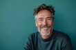 © CogniLens - Portrait of a content caucasian man in his 50s smiling at the camera in front of soft teal background