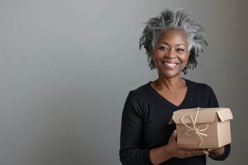 Wall Mural - Portrait of a happy afro-american woman in her 40s holding a box over soft gray background
