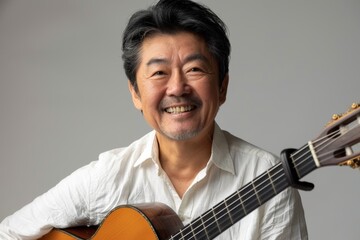 Wall Mural - Portrait of a grinning asian man in his 40s playing the guitar over soft gray background