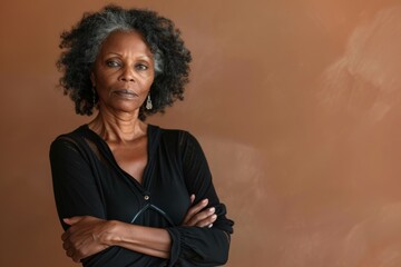 Wall Mural - Portrait of a tender afro-american woman in her 50s with arms crossed on soft brown background