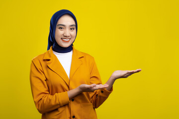 Wall Mural - Happy young Asian woman posing with both hands presenting something isolated on yellow background