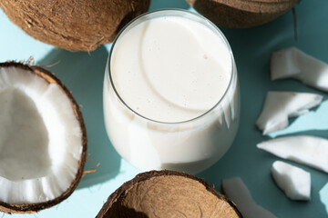 Wall Mural - Coconut milk in a glass among coconuts on a blue background