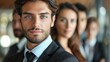 © Tanakorn - Portrait of a young businessman in a suit with a blurred background of colleagues in a corporate setting, exuding professionalism and confidence.