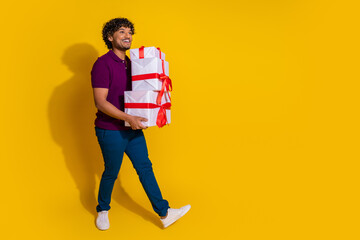 Sticker - Full body photo of attractive young man hold pile gifts walking dressed stylish violet clothes isolated on yellow color background