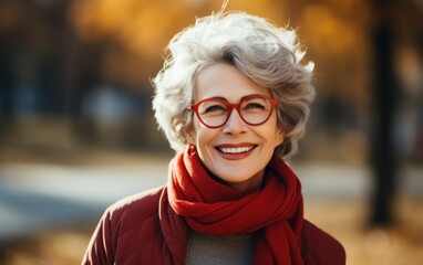 Wall Mural - A woman with red glasses and a red scarf is smiling. She looks happy and content. Concept of warmth and positivity