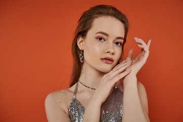 Wall Mural - Woman poses in front of orange backdrop, silver top shining.