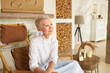 © Anatoliy Karlyuk - Side view of happy senior wealthy lady house owner sitting in chair of boho style room and looking at copy space for your advertising content. Female fashion, furniture, decoration and interior design