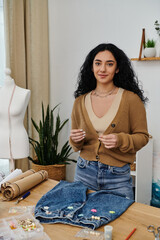 Wall Mural - Young woman upcycles clothes, standing at table by mannequin.