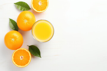 A glass of orange juice with whole oranges and leaves on a white wooden surface