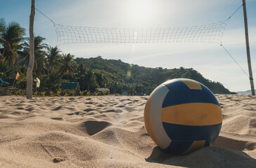 A volleyball rests on the sandy beach beneath a clear, sunny sky.