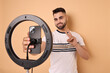 © New Africa - Blogger recording video with smartphone and ring lamp on beige background