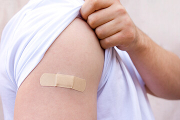 plaster on a man's shoulder. the man pulls up the sleeve of his t-shirt.